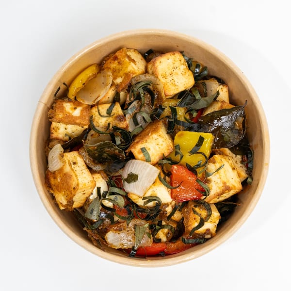 Indian paneer dish with bell peppers, onions, and herbs in a brown bowl.