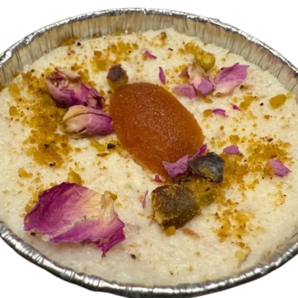 Indian dessert in a foil container, topped with rose petals, orange jam, and pistachio crumbles.