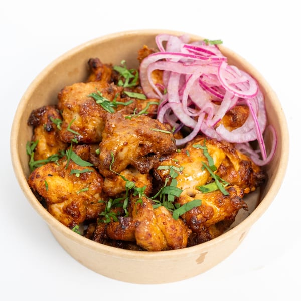 H1B's chicken tikka, garnished with fresh cilantro and red onion, served in a bowl.
