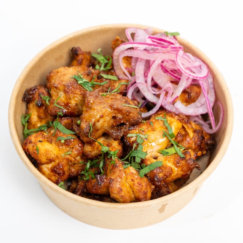 H1B's chicken tikka, garnished with fresh cilantro and red onion, served in a bowl.