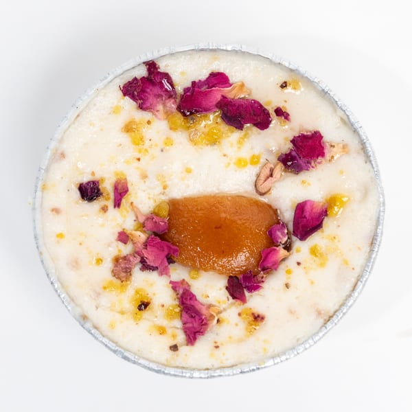 Overhead view of an Indian dessert with rose petals and a gulab jamun in a foil cup.