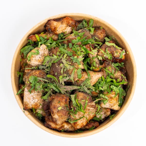 A bowl of H1B's Indian chicken dish, garnished with fresh green herbs and black pepper.