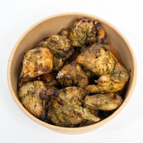 Close-up of green-marinated chicken tikka pieces with charred edges in a round, brown paper bowl.