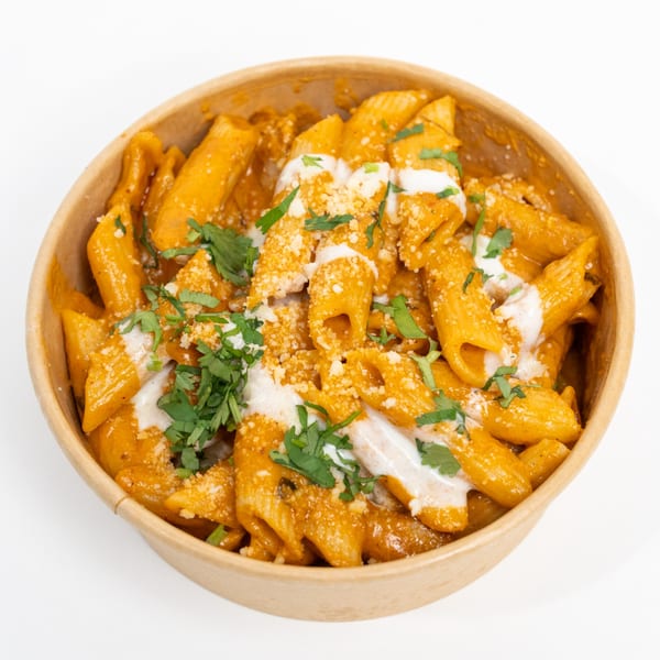 Penne pasta in a creamy orange sauce, topped with white drizzle, grated cheese, and fresh cilantro.