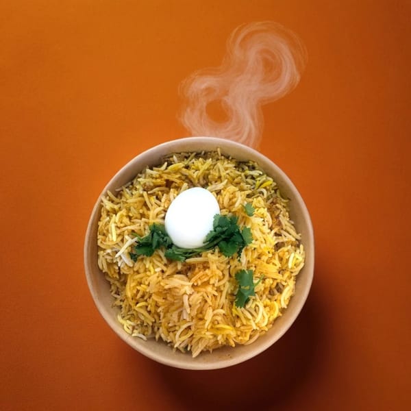 Steaming Hyderabad No1 Biryani with a boiled egg and cilantro in a bowl on an orange background.